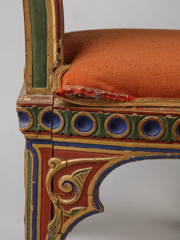 Detail van een Moorse stoel van de zijkant met hout en vergulding met ontbrekende stukjes van de gelijmde, houtgesneden decoraties, van de afwerklaag en schade aan de poten.