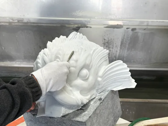 Een hand met handschoen vijlt een marmeren dolfijnenkop