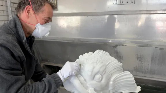 Beeldhouwer met handschoen en mondmasker bewerkt marmeren dolfijnenkop