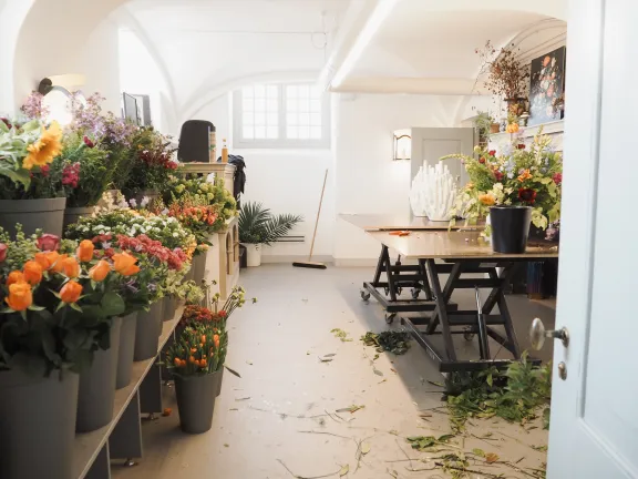 Overzicht van de Bloemenkamer met kleurrijke bloemen in potten en bakken, opgesteld rond een werkbank in een historische binnenruimte.