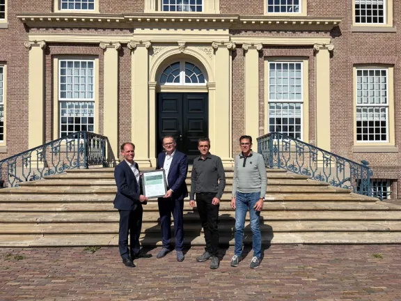 Vier personen houden certificaat vast voor bordes paleis