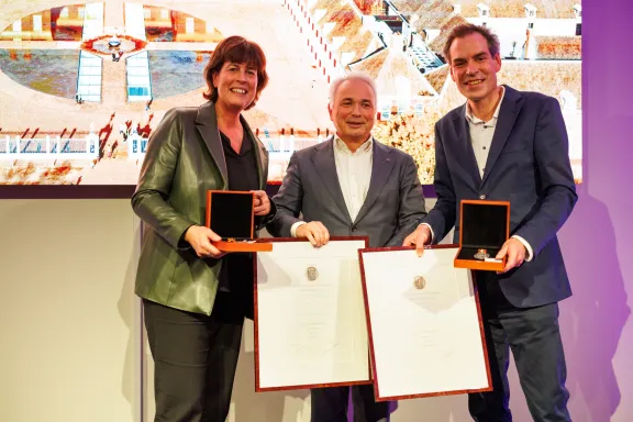 Drie mensen poserend met akte en erepenningen