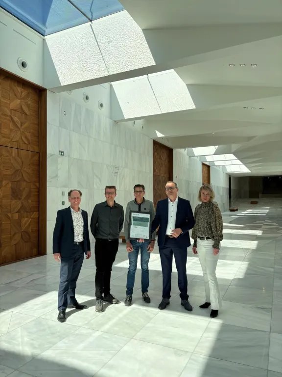 Vijf mannen poseren met BREEAM certificaat in de wit marmeren grand foyer