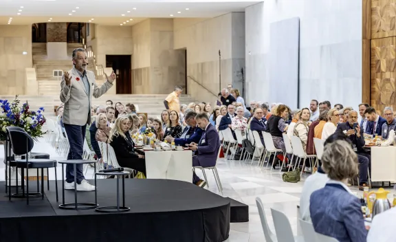 Directeur Frans van der Avert op een podium bij vrijheidsontbijt met mensen aan lange tafels