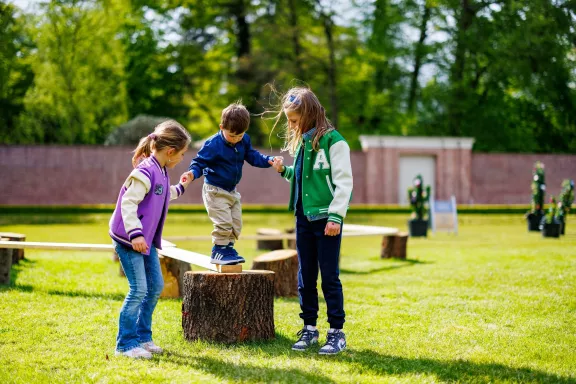 A child helped by two children balances on the balance flower