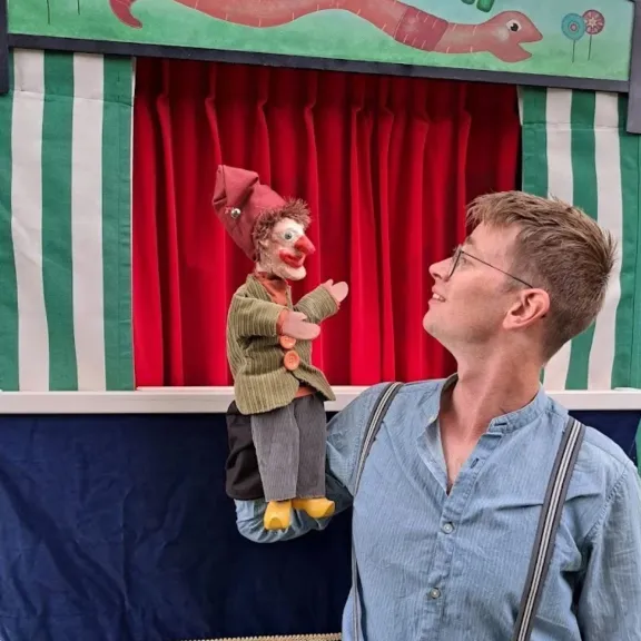 Poppenspeler Klaas-Herman Duursema van Poppentheater Pierewaai met een Jan Klaassen-handpop bij zijn groen-witte poppenkast.