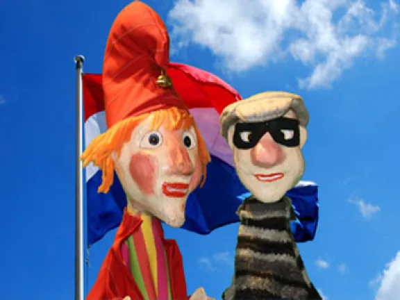 Poppen van Jan Klaassen en een boef met op de achtergrond de Nederlandse vlag en de blauwe lucht