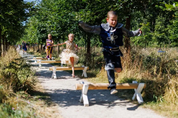 Drie kinderen verkleed als prins, prinses en cheerleader springen over de hordes van het paardenparcours