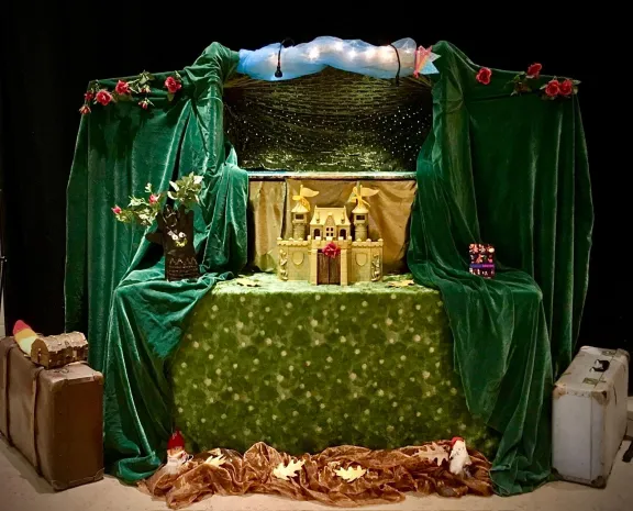 Poppenkast met roze bloemen, koffers, groene colissen en een geel kasteel in het midden