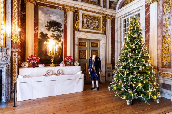 Een tafel in de grote zaal is gedekt in kerstsferen met ernaast een kerstig kostuum en een kerstboom