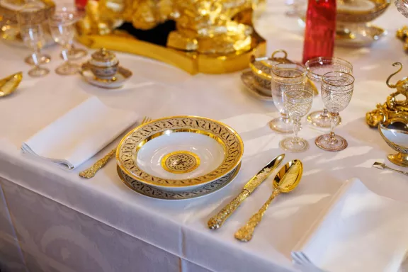 Een gedekte tafel met gouden bestek, glazen, schaaltjes en een bord versierd met gouden randen