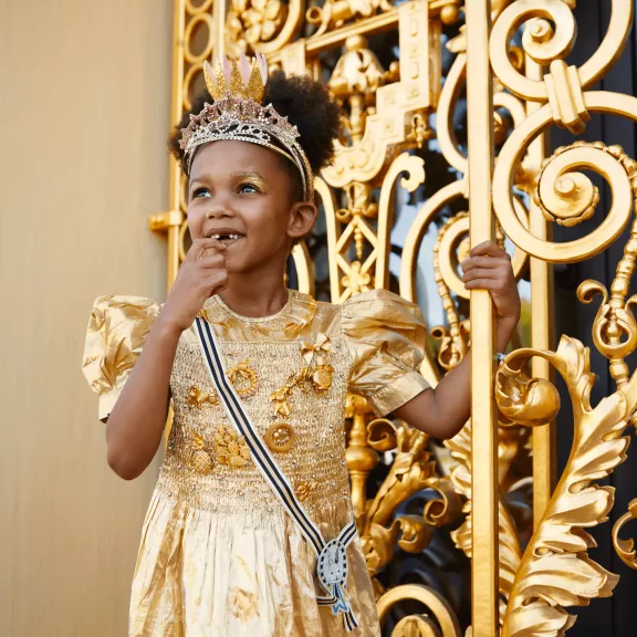 Als Prinzessin gekleidetes Kind hält das goldene Tor des Hintereingangs zum Het-Loo-Palast