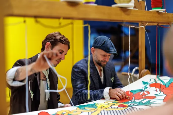 Mannen werken aan een tapijt in het atelier van de tentoonstelling Bloom