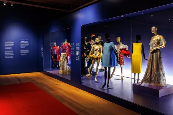 Verschillende feestkostuums van de Toppers, Wilhelmina, een harlekijn, de Lauren Ralph Lauren 'Petra' cocktailjurk in de kleur lichtblauw valt met elegante, golvende cape-mouwen, de Brandon Maxwell-jurk die Meghan Markle droeg en de jurk van Iris van Herpen die met complexe, gelaagde patroon dat met innovatieve technieken is gemaakt.