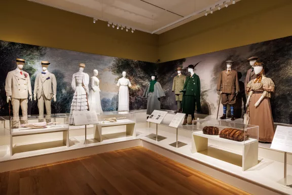 Verschillende buitenkleding kostuums. Pakken van mannen in wit en beige met zonnehoeden, witte japons en ook kostuums in verschillende kleuren groen en bruin voor buiten gemaakt van materialen geschikt voor buiten zoals tweed