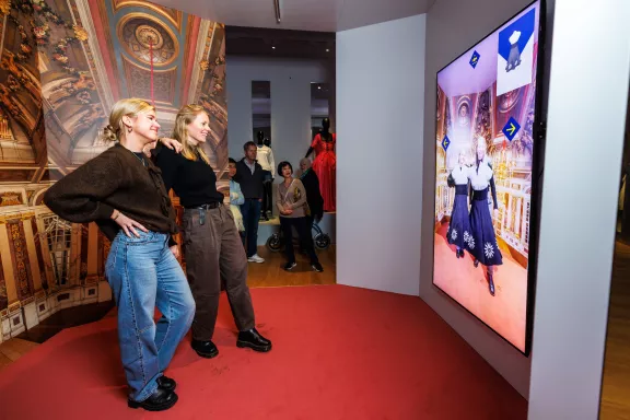 Twee vrouwen proberen lachend de digitale paskamer uit als onderdeel van de tentoonstelling Dresscodes