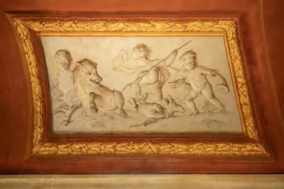 Reliëfs geschilderd in grijstinten. Ze tonen naakte figuurtjes, putti genoemd, die bezig zijn met de jacht