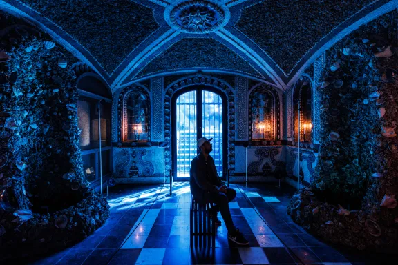 Een man zit op een bankje in de schelpengrot te kijken naar het kunstwerk Biophony of Het Loo