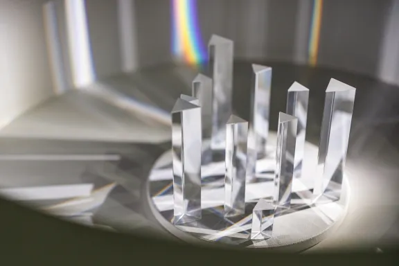 Glasprismen auf einem runden weißen Sockel brechen das Licht in Regenbogenfarben in der Ausstellung Weiß, mehr als eine Farbe.