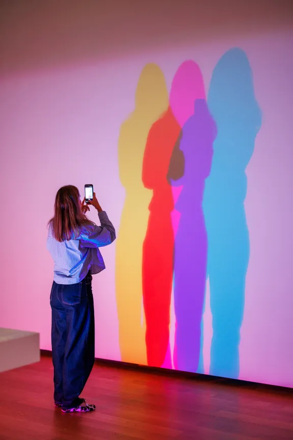 Bezoeker fotografeert kleurrijke schaduwen die ontstaan door gekleurd licht in de tentoonstelling Wit, meer dan een kleur.