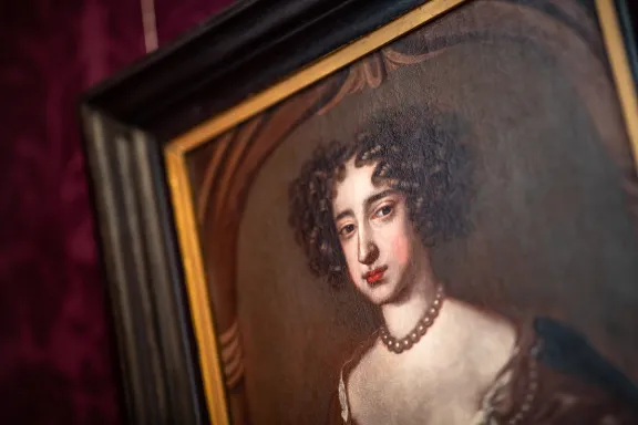 Een schilderij van Mary II Stuart met donkere krullen, rode lippen, kralenketting en een witte huid