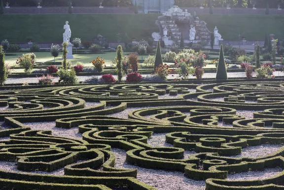 Buxus haag in symmetrische barok parterres, met struiken en bloemen daar achter, en beelden zoals de narcisus cascade op de achtergrond